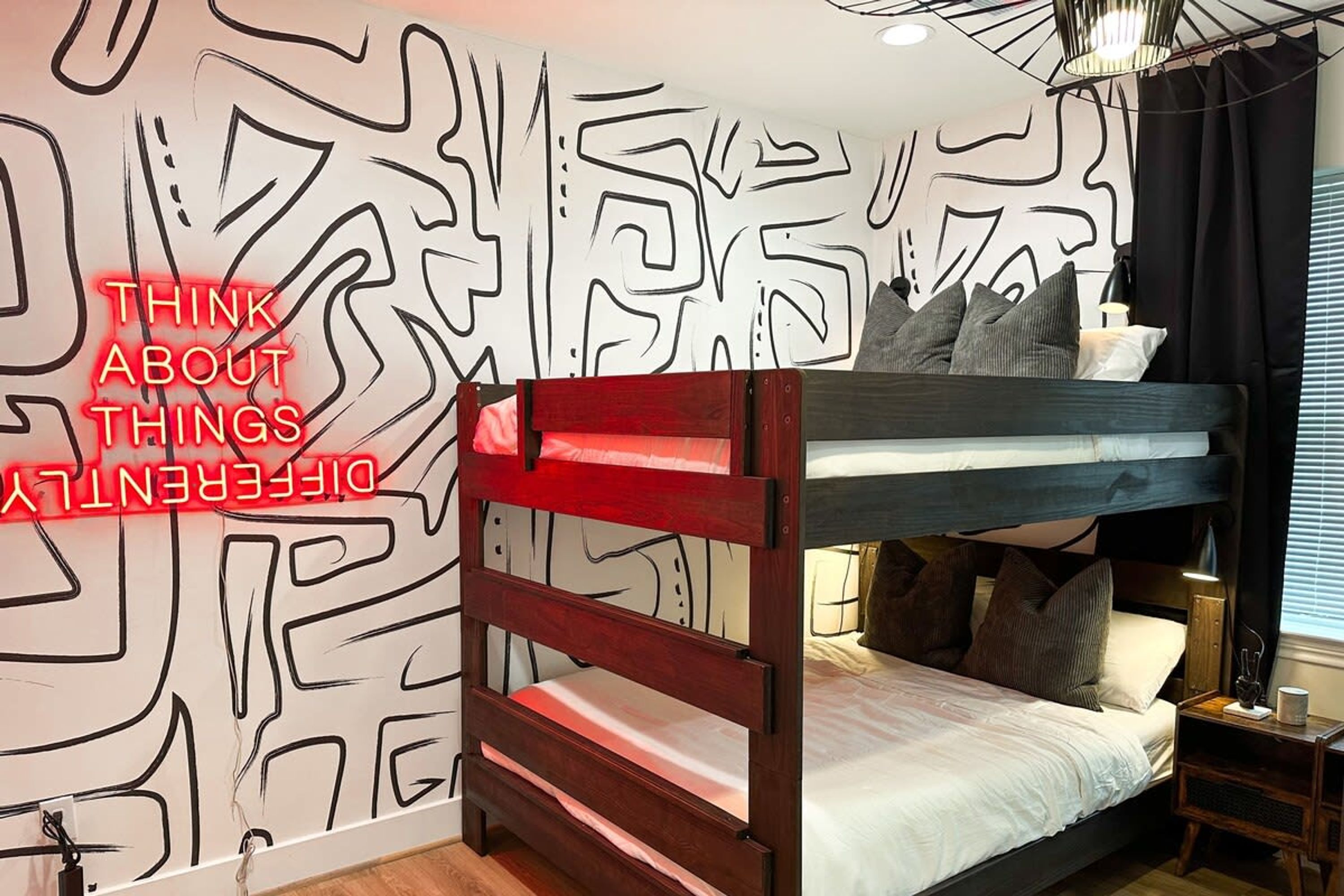 Habitación con literas, un diseño geométrico en la pared, una mesita de noche y una lámpara.
