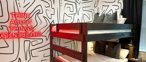 Habitación con literas, un diseño geométrico en la pared, una mesita de noche y una lámpara.