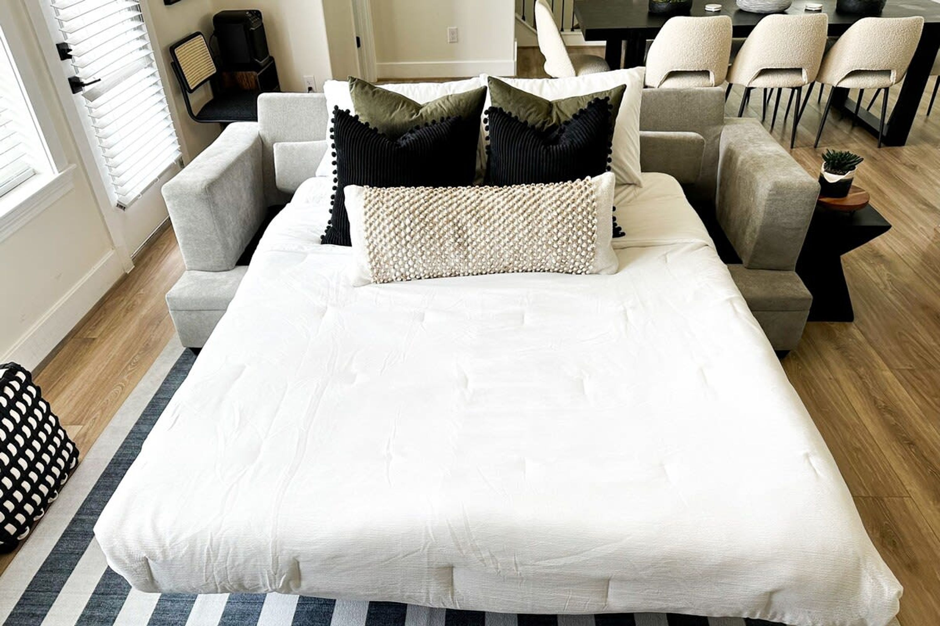 Ein modernes Schlafzimmer mit einem großen Bett, einem grauen Sofa und einer Essecke mit Stühlen.