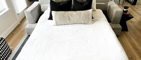 Ein modernes Schlafzimmer mit einem großen Bett, einem grauen Sofa und einer Essecke mit Stühlen.