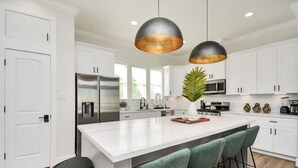 A modern kitchen with white cabinets, stainless steel appliances, and a central island with bar stools. - Paradise Palace Best Rooftop in HTX w Hot Tub (Houston)