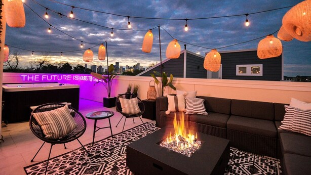A rooftop patio with a fire pit, outdoor seating, string lights, and a city view. - Paradise Palace Best Rooftop in HTX w Hot Tub (Houston)
