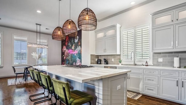A modern kitchen with white cabinets, a large island with a sink, and pendant lighting. - Urban Jungle Retreat in the HTX Skyline (Houston)