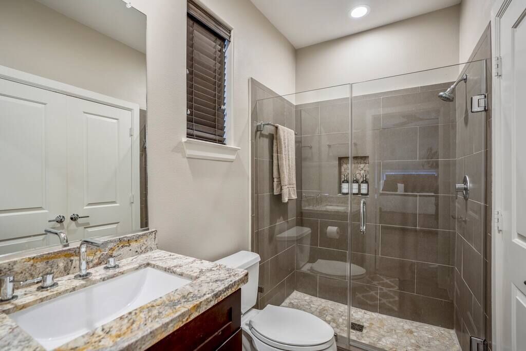 Une salle de bain avec un lavabo en marbre, des toilettes et une douche séparée par une paroi de verre.