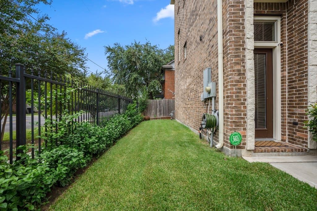 A well-maintained backyard with a brick house, a wooden fence, and a lawn.