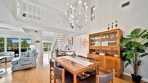 A spacious living area with a dining table, chairs, a staircase, and a large plant.