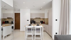 A modern kitchen with white cabinetry, a wooden dining table with two chairs, and a built-in oven. - Maison Privee - Modern & Chic Retreat 10min from Downtown Dubai (Dubai)