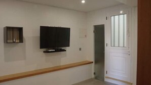 Et værelse med et fladskærms-tv monteret på væggen, en træbænk langs den ene væg, og en hvid dør med frostet glas.
