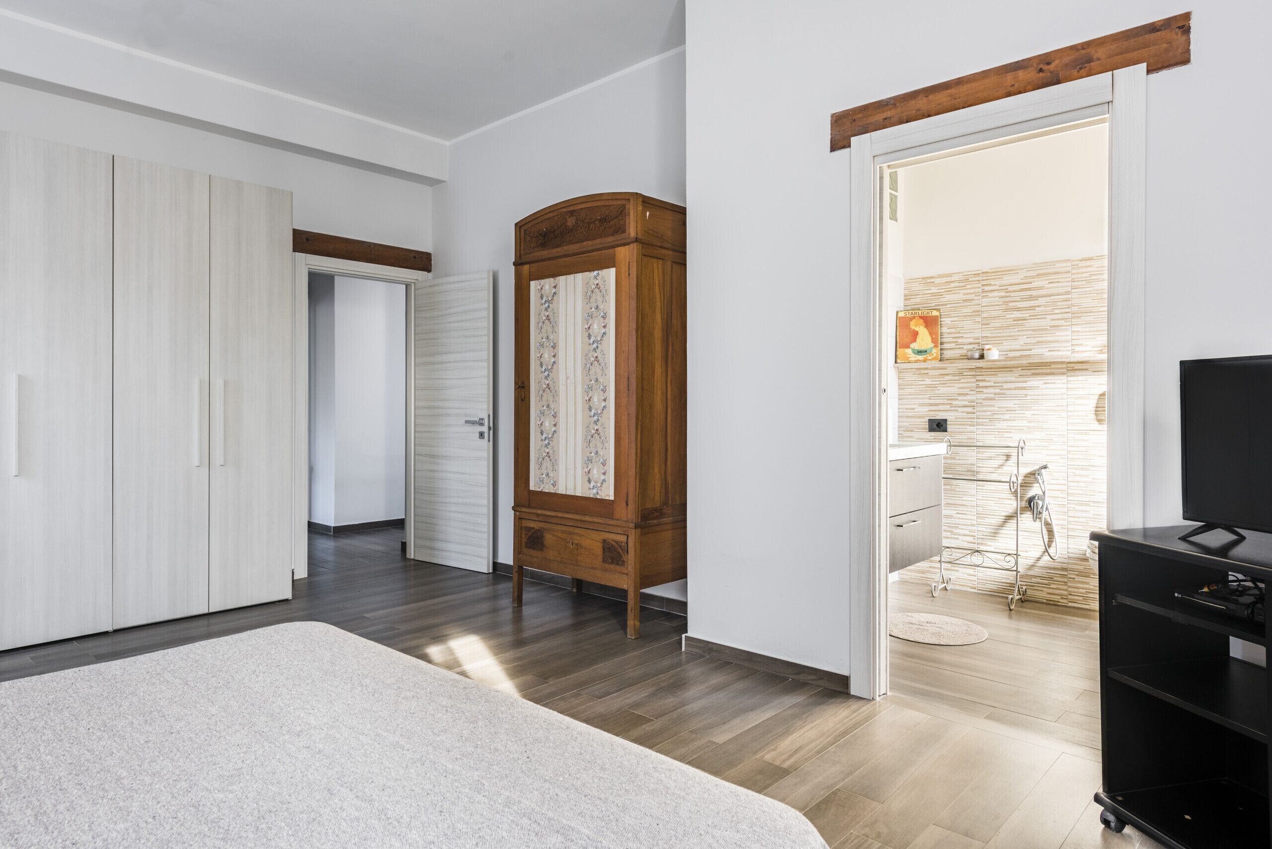 A bedroom with a large bed, a wardrobe, a wooden cabinet, and a TV stand.