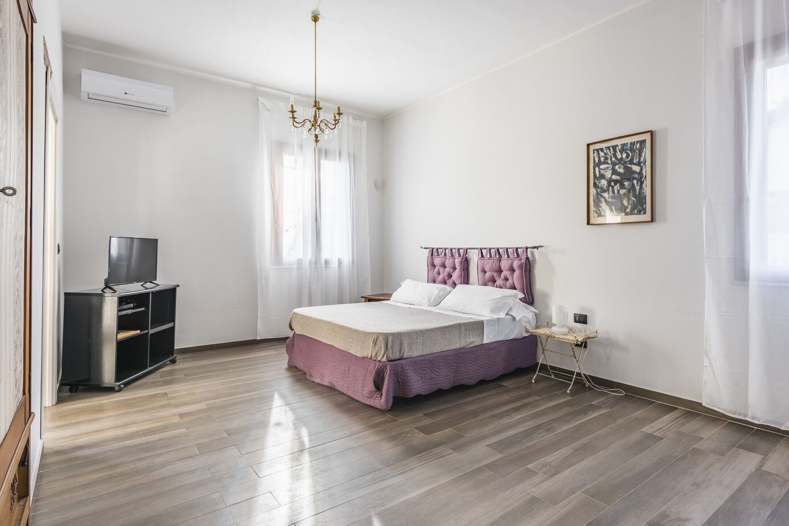 A bedroom with a bed, a TV stand, a bedside table, and a window with curtains.