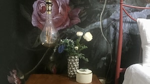 Une table de chevet en bois, ornée d’un vase de fleurs et d’une lampe.