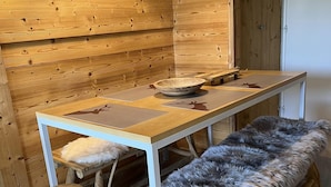 Un intérieur en bois avec une table, des tabourets et un banc recouvert de fourrure.