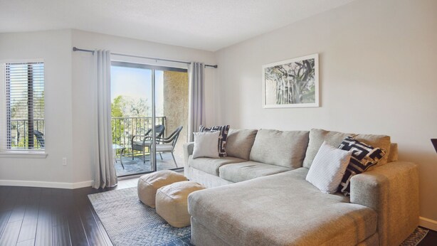A living room with a grey sofa, ottomans, a patterned rug, a balcony with outdoor furniture, and a framed picture on the wall. - Beautifully Furnished 2BR/2Bath Unit 5th Floor Gem - 1 Block from the Beach (Hilton Head Island)