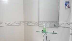A bathroom with a white sink, a mirror, and a glass shelf with a green bottle.