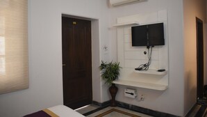 A hotel room with a bed, a television mounted on the wall, an air conditioning unit, a door, and a potted plant.