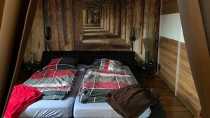 A room with a bed featuring a red and grey checkered bedspread, a brown throw blanket, and a wooden wall paneling design. - 2 Zimmer Wohnung/zentral/bayernähe! (Leverkusen)