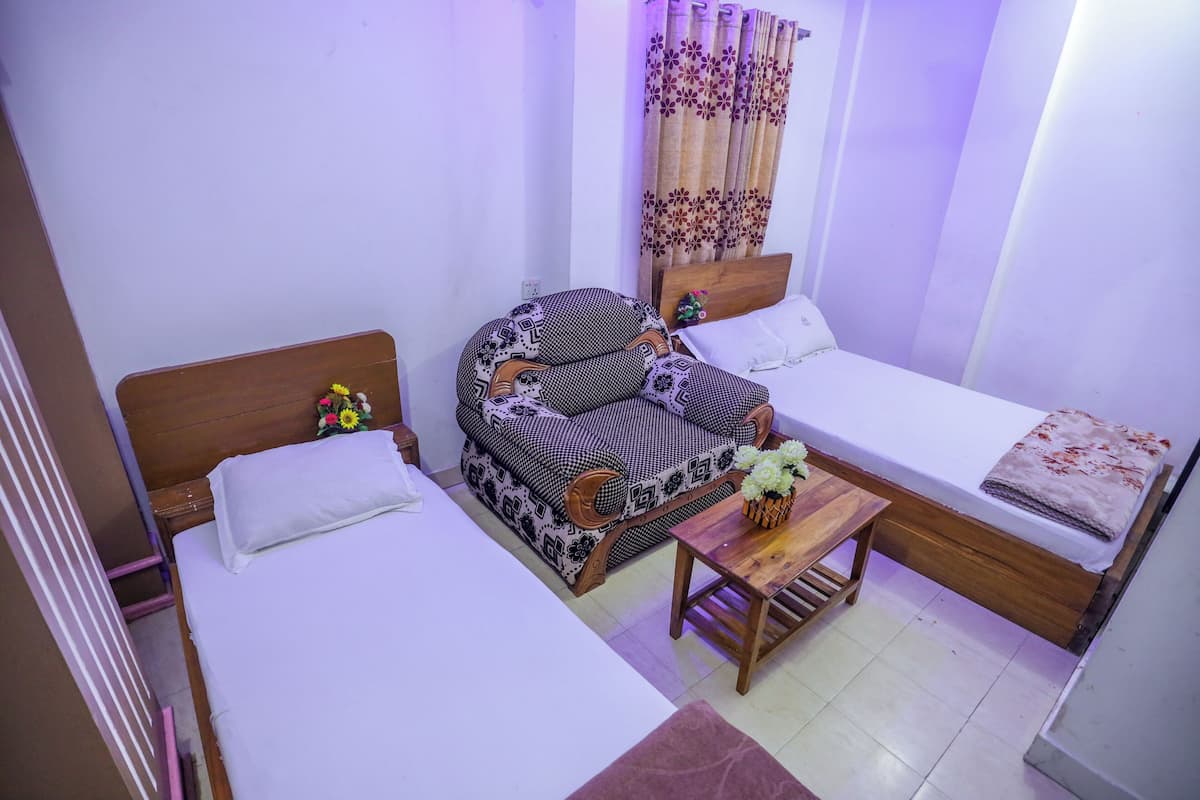 A room with two single beds, a sofa, a wooden table, and a curtain with a floral pattern.