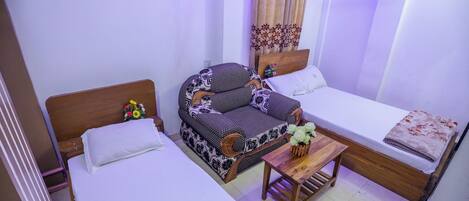 A room with two single beds, a sofa, a wooden table, and a curtain with a floral pattern.