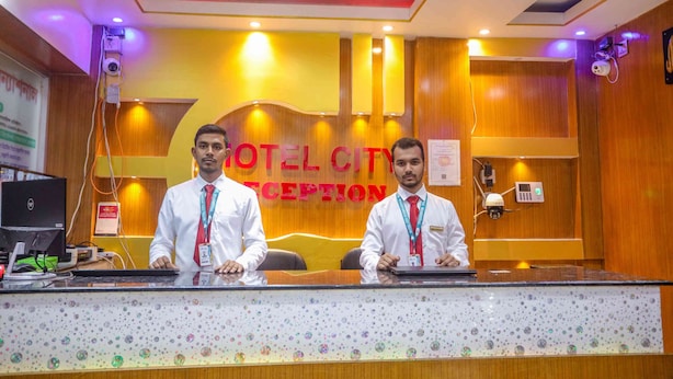 Ein Empfangstresen mit zwei Mitarbeitern, ein Holzbüro, ein Computer und ein Schild mit der Aufschrift 'HOTEL CITY RECEPTION'.