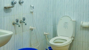 Ein Badezimmer mit Toilette, Waschbecken und Dusche. Auf dem Boden stehen zwei blaue Eimer.
