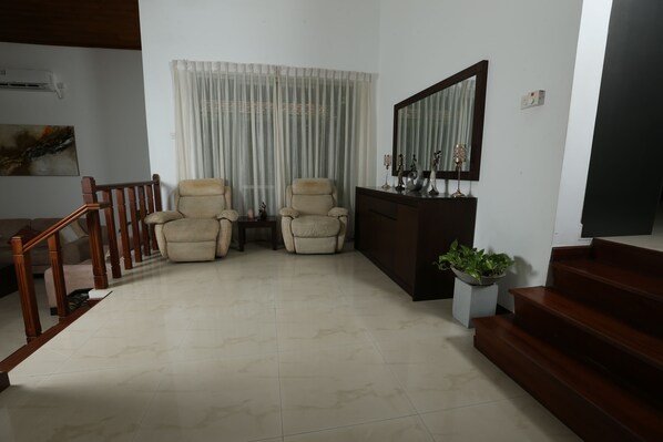 A living room with a wooden staircase, two beige armchairs, a dark wooden cabinet, a potted plant, and a large mirror on the wall. - 428/89 (Thalawatugoda)