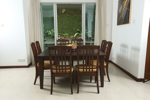 A dining area with a round table and six chairs, a small fruit bowl, and a view of a garden through glass doors. - 428/89  (Thalawatugoda)