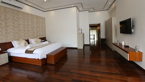 Een moderne hotelkamer met een groot bed, houten vloeren, een plafondventilator, een flatscreen televisie en een ingebouwde bank.