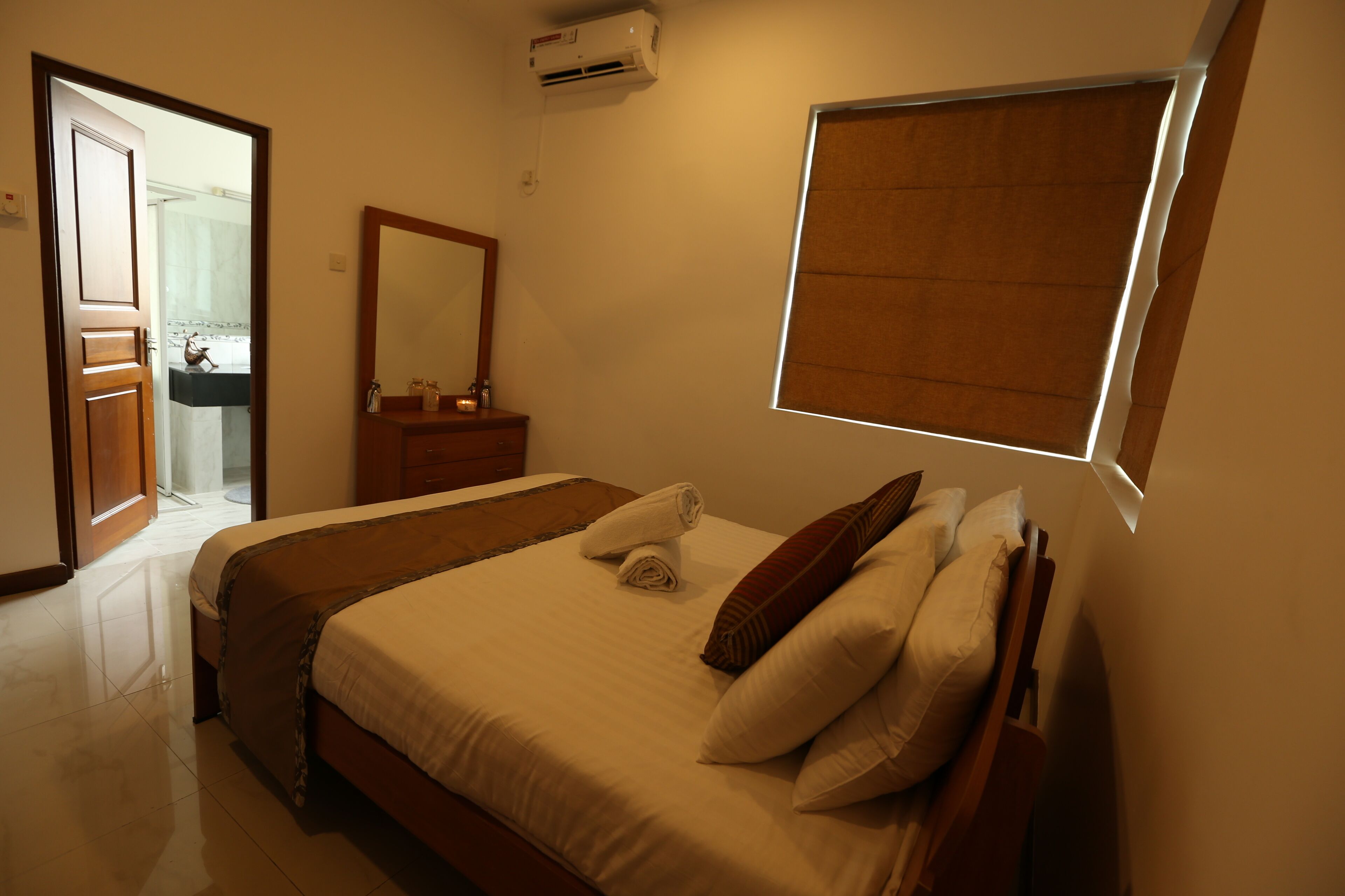Quarto de hotel com cama, penteadeira, espelho e janela com persianas.
