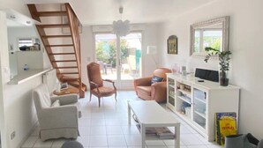 A living room with a staircase, a sofa, a coffee table, and a TV stand. - Maison Avec Plages et Commerces à Pieds (Batz-sur-Mer)