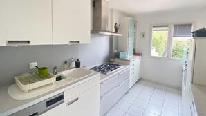 A modern kitchen with white cabinets, a gas stove, and a window with blinds. - Maison Avec Plages et Commerces à Pieds (Batz-sur-Mer)