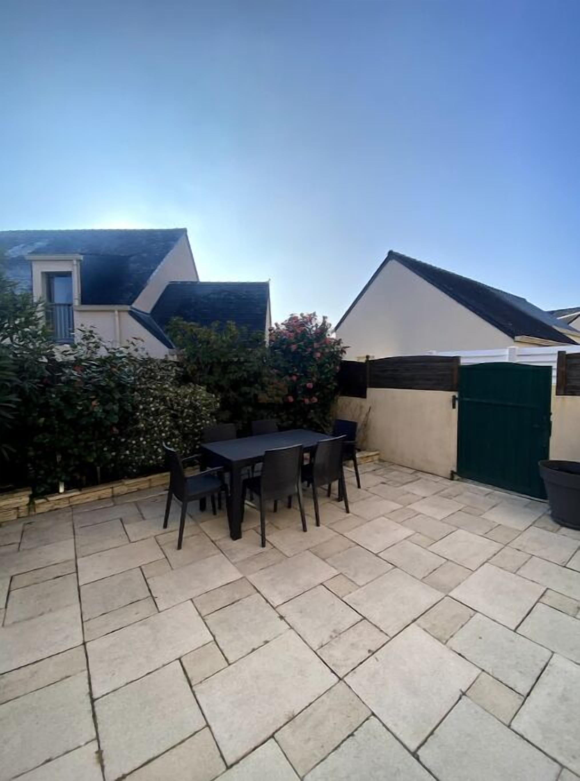 A patio with a table and chairs, surrounded by a low wall and a green gate.