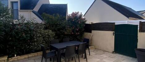 A patio with a table and chairs, surrounded by a low wall and a green gate.