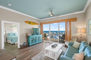 Een woonkamer met uitzicht op de oceaan, een plafondventilator, een televisie en een turquoise bank.