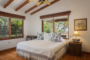 A bedroom with a bed, two windows, a wooden ceiling, a nightstand, and a lamp. - Casa Encantos Beach Front House (Hacienda Iguana)