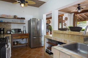 A modern kitchen with a stainless steel refrigerator, microwave, and stove. There are shelves with dishes and a large sink.