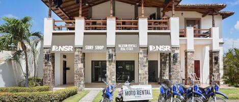 Un edificio con letreros para una tienda de surf, alquileres vacacionales y un servicio de alquiler de motos.