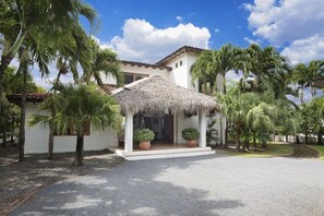 A white building with a thatched-roof structure in front, surrounded by palm trees. - Casa Encantos Beach Front House (Hacienda Iguana)
