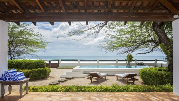 Ein Poolbereich mit Blick aufs Meer, umgeben von Grünpflanzen und einer Pergola.
