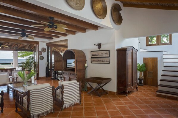 A spacious living area with a view of the ocean, wooden furniture, and a ceiling fan.