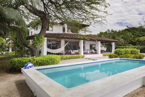 A poolside area with a white building, a hammock, and a clear blue pool.