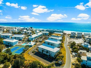 An aerial view of a coastal resort with multiple buildings, a tennis court, and a beach. - Beachside Dream 121-Tennis Court-Sleeps 10 (Santa Rosa Beach)