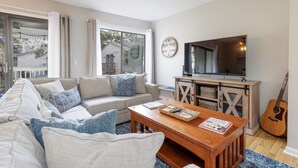 A living room with a sofa, coffee table, TV, and guitar. - 54 Forest Gardens: Serene and Relaxing Villa, Walk to Beach, Pool, Free Bikes (Hilton Head Island)