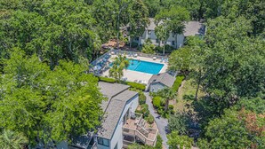 An aerial view of a resort with a swimming pool surrounded by lush greenery and a building with a curved roof. - 54 Forest Gardens: Serene and Relaxing Villa, Walk to Beach, Pool, Free Bikes (Hilton Head Island)