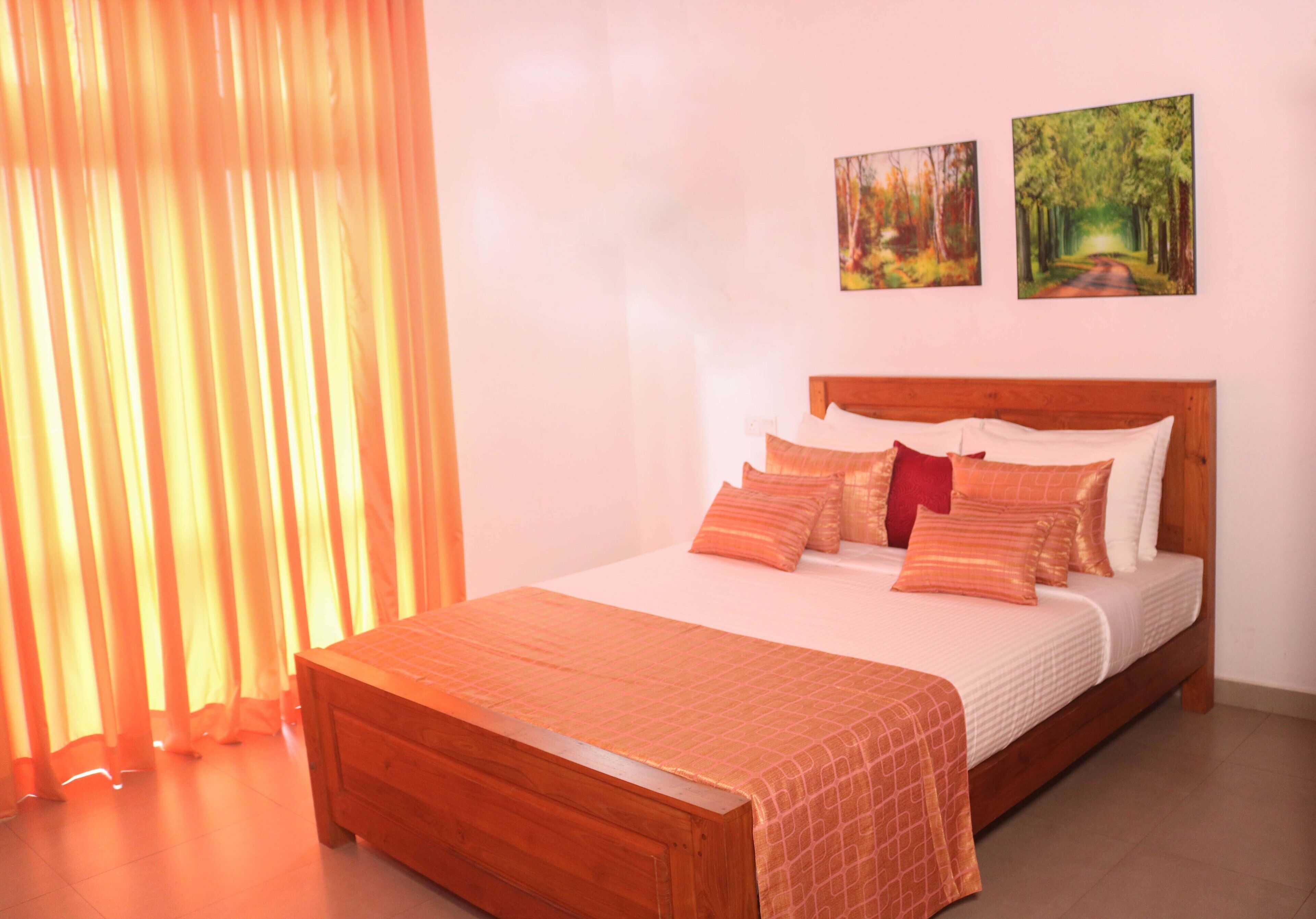Une chambre à coucher avec un lit en bois, une literie orange et deux tableaux représentant des paysages accrochés au mur.