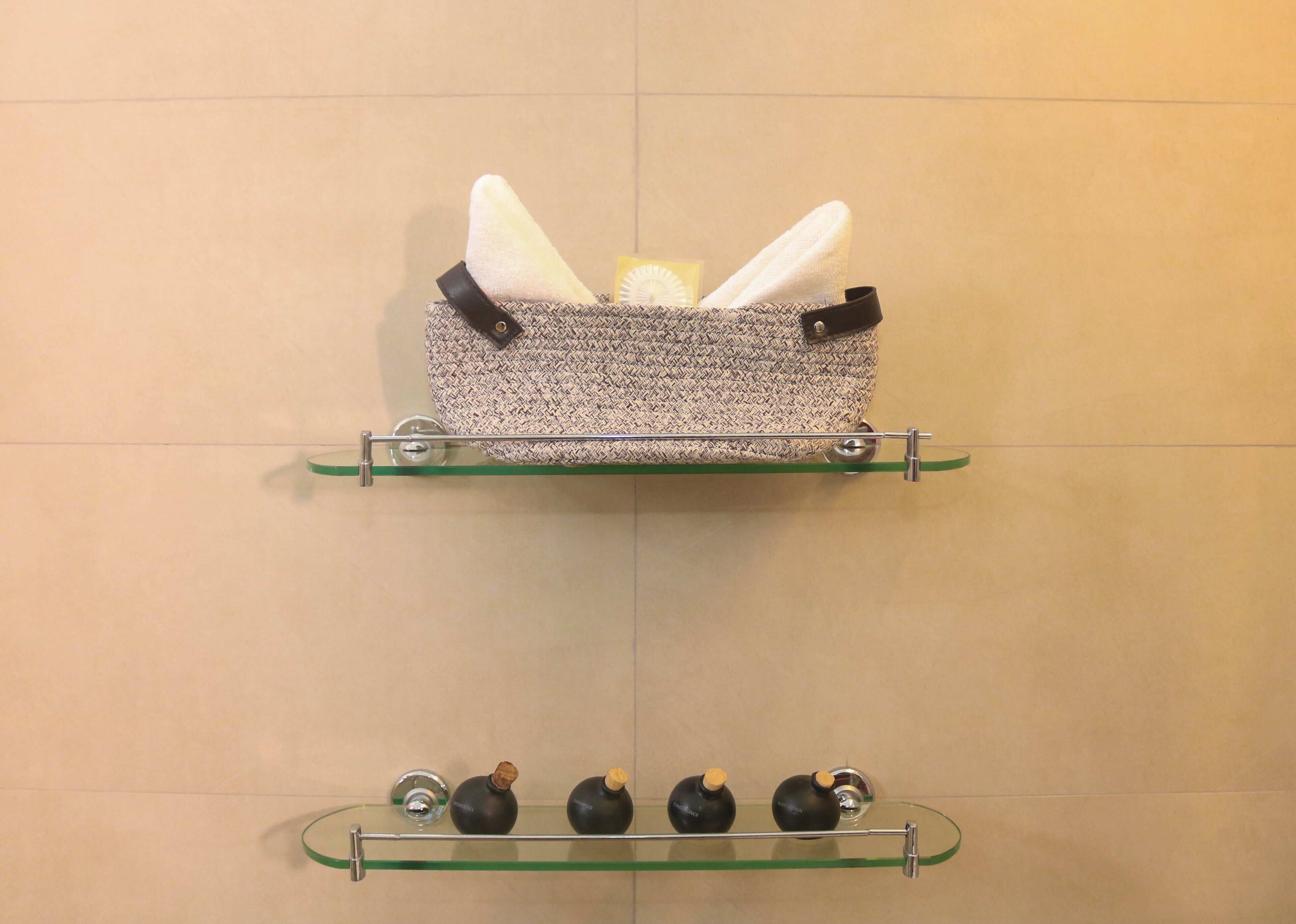 A bathroom with a towel rack holding a patterned towel and a toiletry bag, and a shelf with three black bottles.
