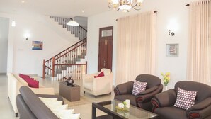 Un salon spacieux avec un escalier, deux canapés, une table basse et un lustre.