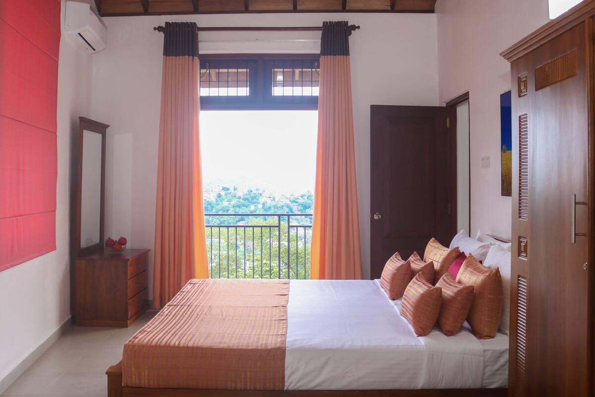 A bedroom with a bed, a dresser, a mirror, and a balcony with curtains.
