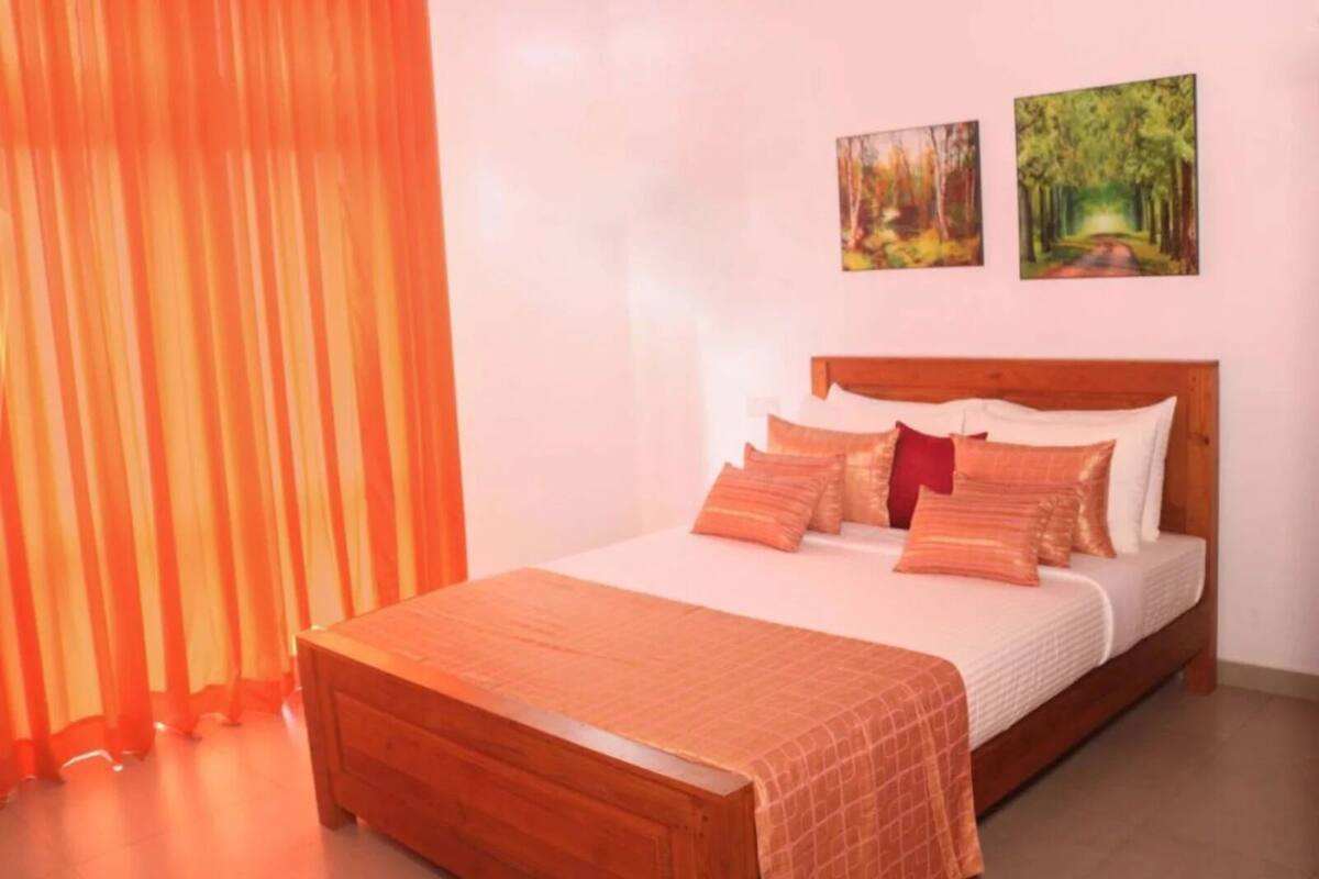 A bedroom with a wooden bed, orange curtains, and two paintings on the wall.