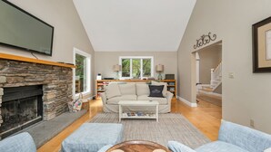 A living room with a stone fireplace, a sofa, a coffee table, and a bookshelf. - LABOR DAY SPECIAL 2 NIGHTS FREE Lake Winnipesaukee Waterfront Sleeps 14 (Moultonborough)