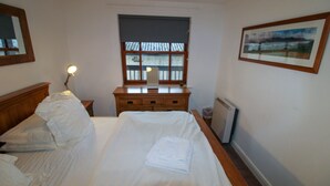 Une chambre à coucher comprenant un lit, une table de chevet, une commode, une fenêtre avec des stores et un tableau encadré accroché au mur.
